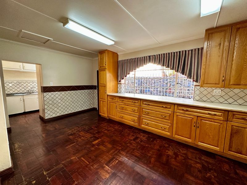 Spacious kitchen featuring traditional wooden cabinetry, parquet flooring, and a tiled splashback, with an adjacent scullery area visible through the doorway.
