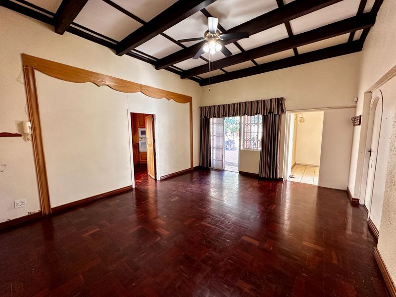 Spacious living room featuring classic parquet flooring, exposed timber ceiling beams, and direct access to an outdoor patio area.