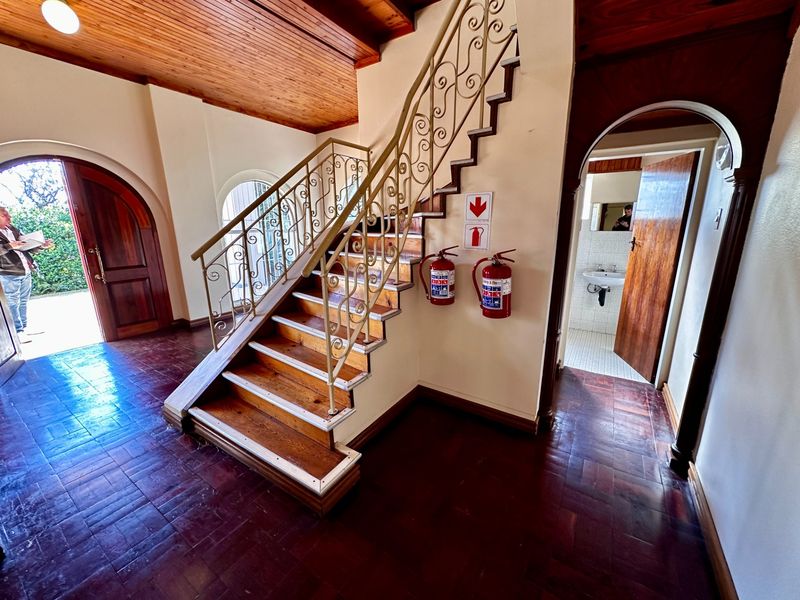 Entrance foyer featuring a wooden staircase with wrought iron balustrade, timber ceiling, and parquet flooring, leading to an adjacent bathroom area.