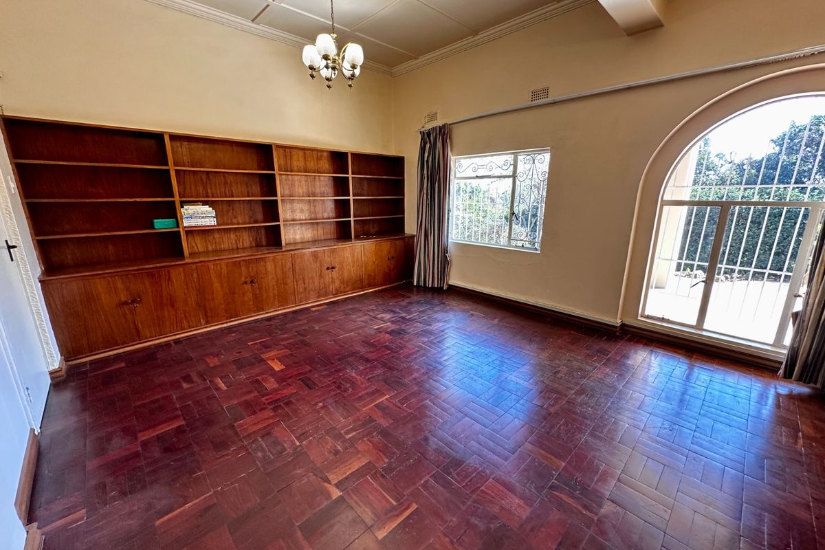 Spacious living area featuring classic parquet flooring, extensive built-in wooden cabinetry, and an elegant arched window with security bars.