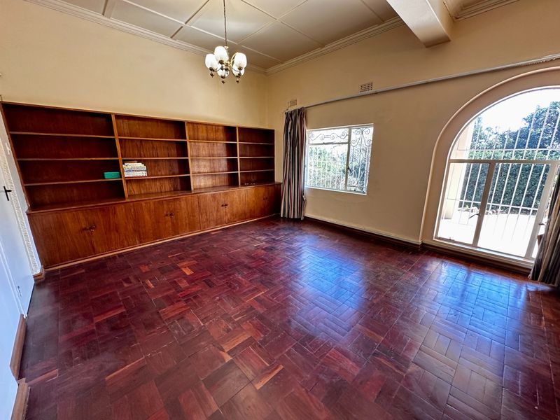 Spacious living area featuring classic parquet flooring, extensive built-in wooden cabinetry, and an elegant arched window with security bars.