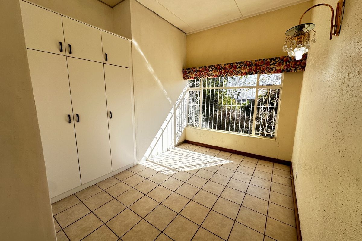 An empty bedroom featuring tiled flooring, built-in cupboards, and a window fitted with security bars.