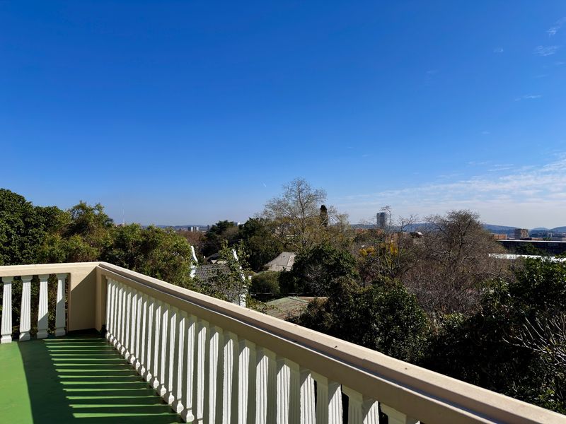 An elevated balcony featuring a white balustrade railing, offering expansive views over the surrounding neighborhood and mature trees.