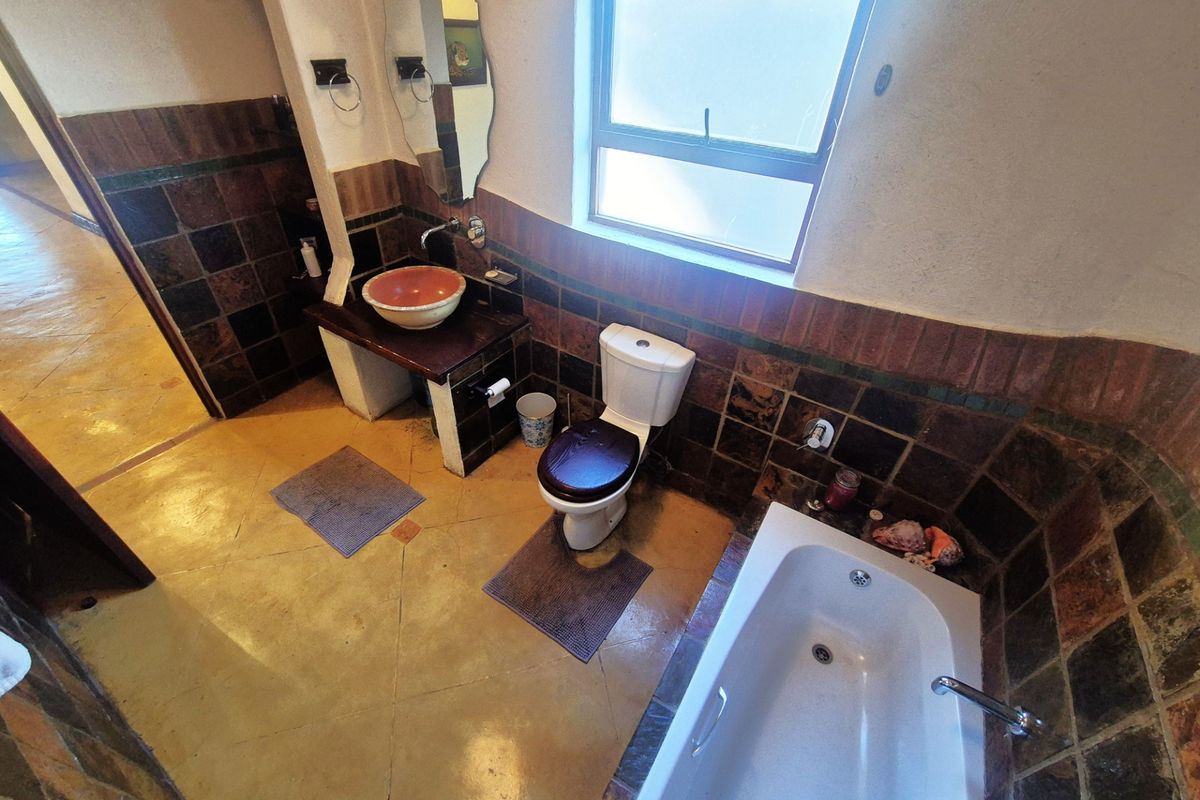 A dated bathroom featuring a vessel sink on a built-in vanity, a standard toilet, and a bathtub with dark tiled wall accents.
