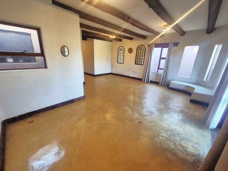 Spacious living area featuring exposed timber ceiling beams, polished concrete flooring, and a built-in window bench with arched window detailing.