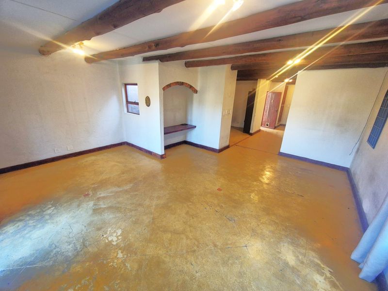 An empty living area featuring exposed timber ceiling beams, a built-in arched wall niche, and painted concrete flooring throughout.
