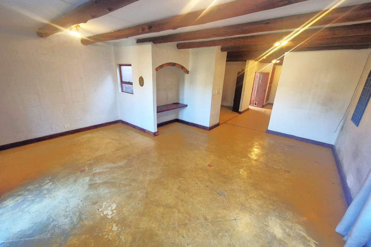 An empty living area featuring exposed timber ceiling beams, a built-in arched wall niche, and painted concrete flooring throughout.