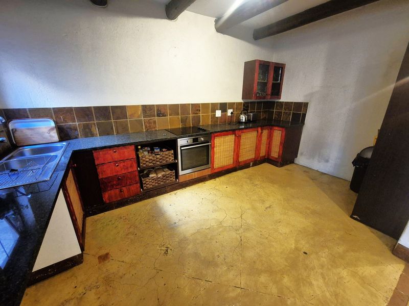 Kitchen featuring dark stone countertops, built-in oven, electric hob, double sink, and exposed ceiling beams with concrete flooring.