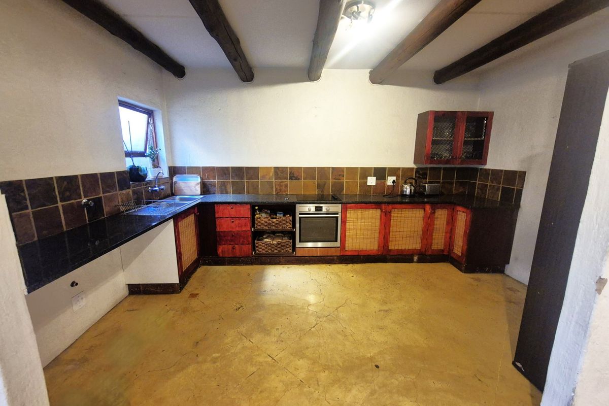A rustic kitchen featuring exposed timber ceiling beams, granite countertops, built-in oven, and tiled backsplash, with concrete flooring throughout.