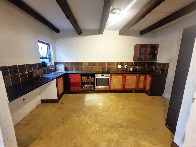 A rustic kitchen featuring exposed timber ceiling beams, granite countertops, built-in oven, and tiled backsplash, with concrete flooring throughout.
