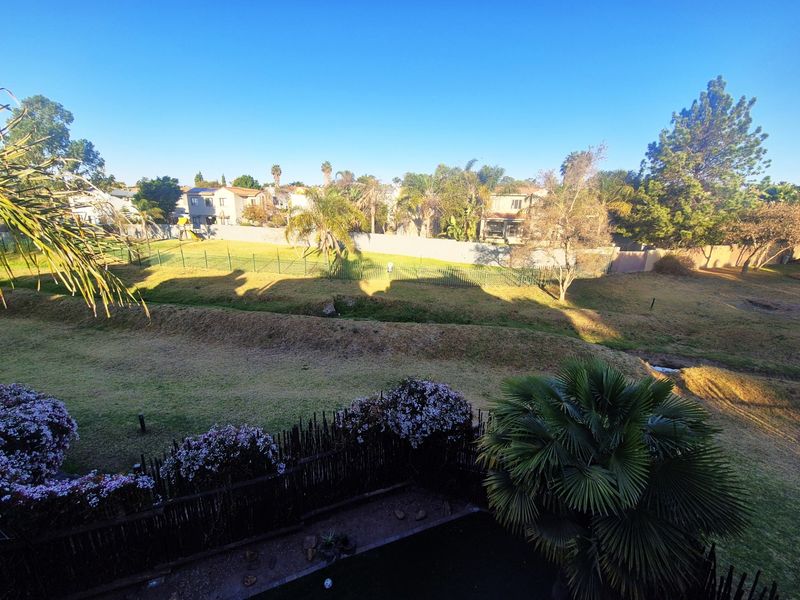 Elevated view overlooking a landscaped communal garden area with established trees and perimeter fencing.
