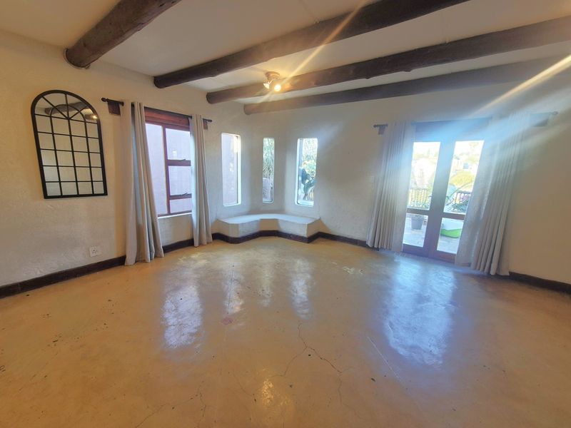 Spacious living area featuring exposed timber ceiling beams, polished concrete flooring with visible cracking, a built-in window seat, and access to an outdoor area.