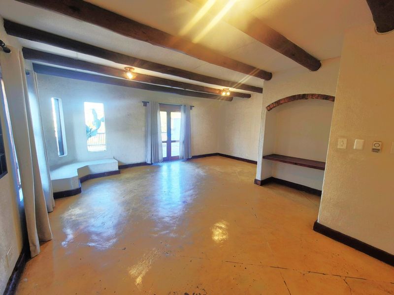 Spacious living area featuring exposed timber ceiling beams, polished concrete floors, a built-in bench, and an arched alcove with direct access to the outdoors.