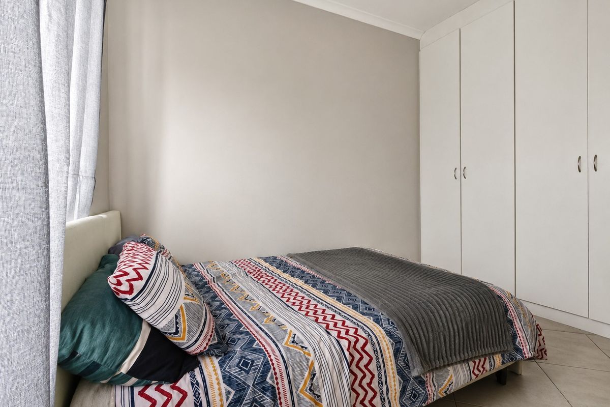 A well-maintained bedroom featuring neutral wall tones, tiled flooring, and ample built-in cupboard storage.