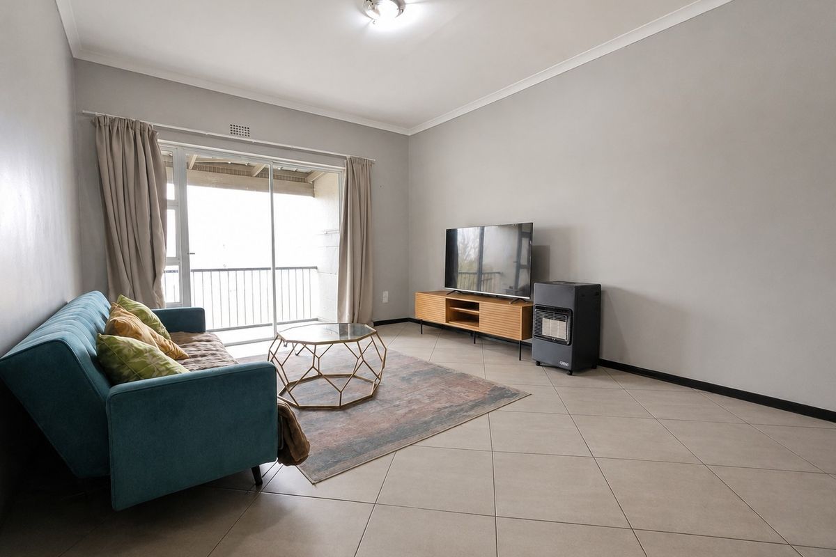 A bright living room featuring neutral tiled flooring, smooth walls, and a sliding glass door providing access to an outdoor balcony area.