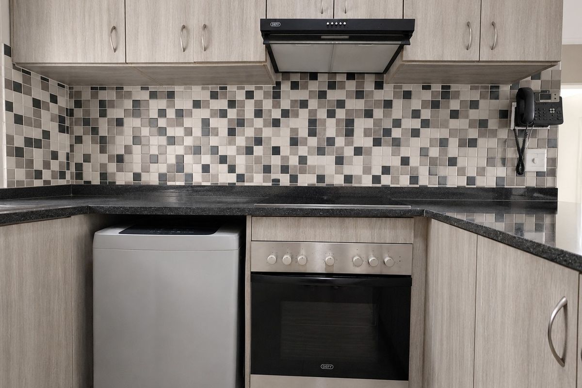 A functional kitchen featuring light wood-grain cabinetry, dark stone-look countertops, a mosaic tile backsplash, and integrated stainless steel oven and extractor fan.