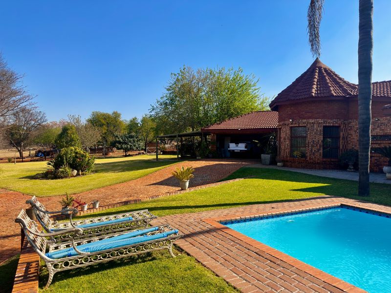 A well-maintained farm property featuring a swimming pool, brick-paved patio area, and a covered carport adjacent to the main brick residence.