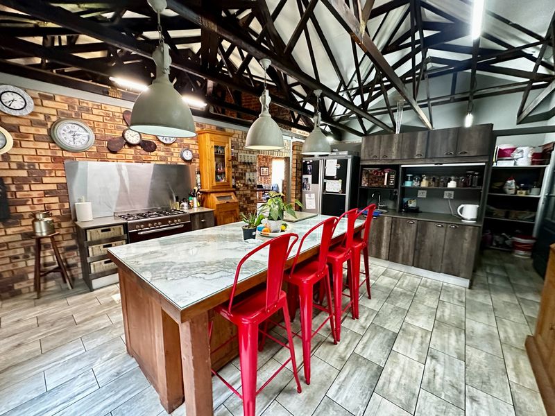 Spacious farmhouse kitchen featuring exposed timber roof trusses, a large central island with stone countertop, exposed brick walls, and modern cabinetry.