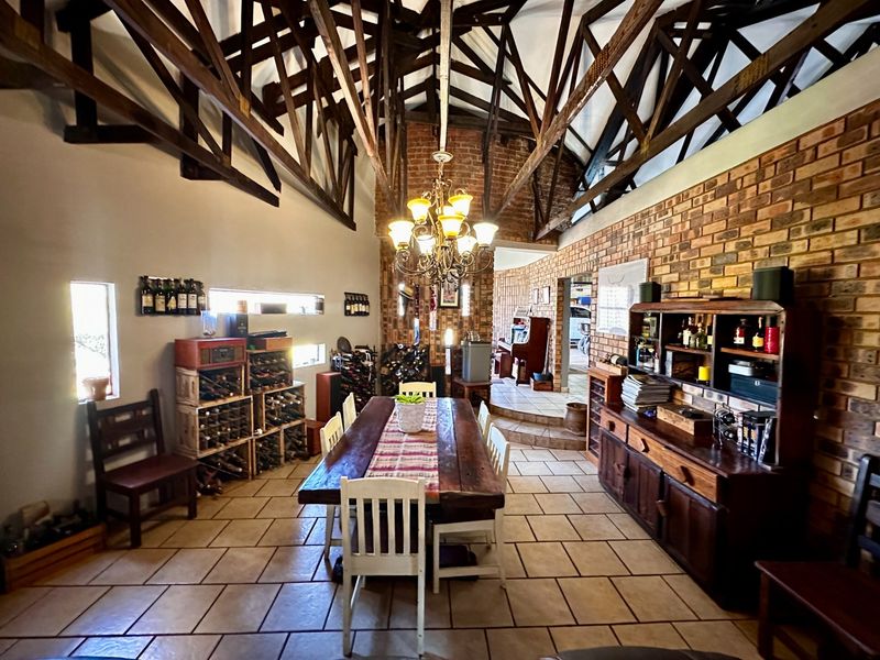 Spacious dining area featuring high vaulted ceilings with exposed timber trusses, rustic exposed brick walls, and durable tiled flooring in a farm-style setting.