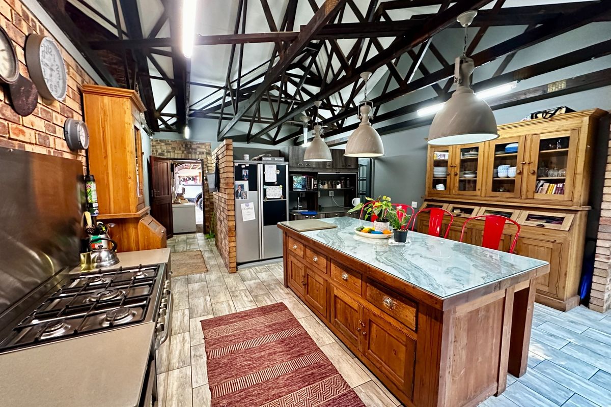 Spacious farmhouse kitchen featuring exposed timber roof trusses, a large central island with stone countertop, gas hob, and extensive built-in wooden cabinetry.