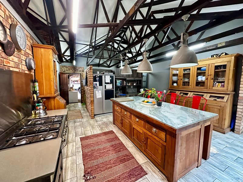 Spacious farmhouse kitchen featuring exposed timber roof trusses, a large central island with stone countertop, gas hob, and extensive built-in wooden cabinetry.