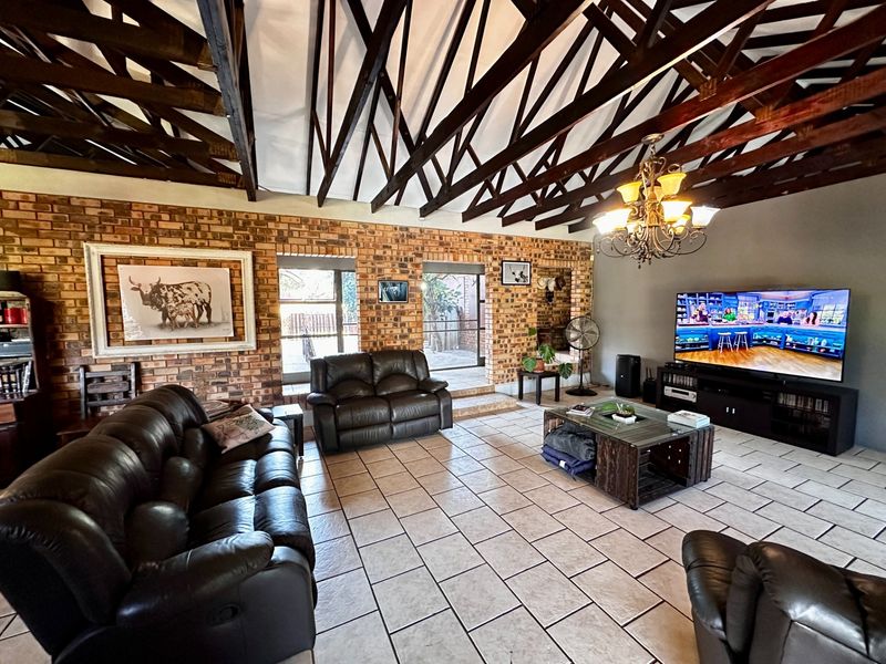 Spacious living room featuring high vaulted ceilings with exposed timber trusses, rustic brick walls, and large sliding doors leading to the exterior.