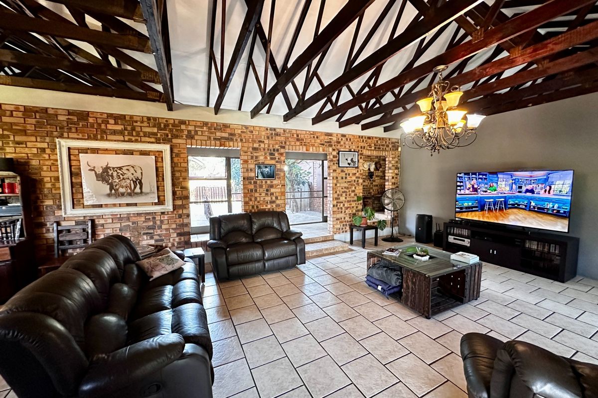 Spacious living room featuring high vaulted ceilings with exposed timber trusses, rustic brick walls, and large sliding doors leading to the exterior.
