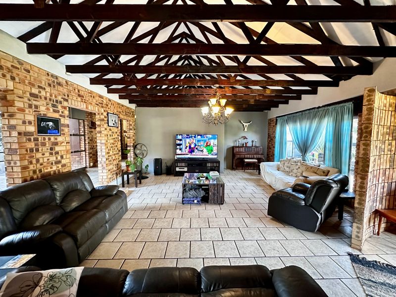 Spacious living room featuring high vaulted ceilings with exposed timber trusses, rustic exposed brick walls, and neutral tiled flooring.