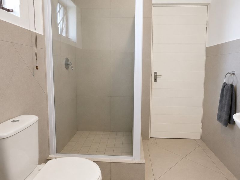 A clean and modern bathroom featuring a glass-enclosed shower, neutral floor-to-ceiling tiling, and a standard toilet.