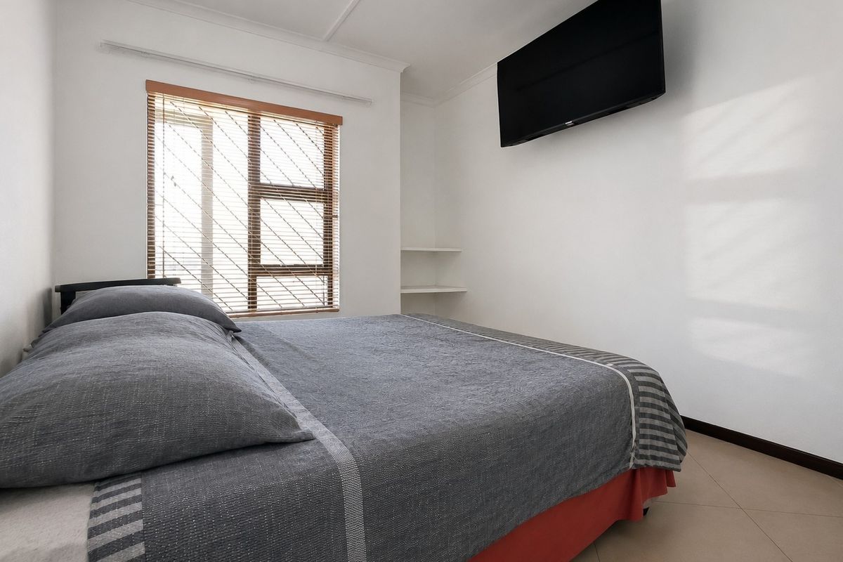 A bedroom featuring tiled flooring, built-in shelving, and window blinds, providing a functional and neutral space.