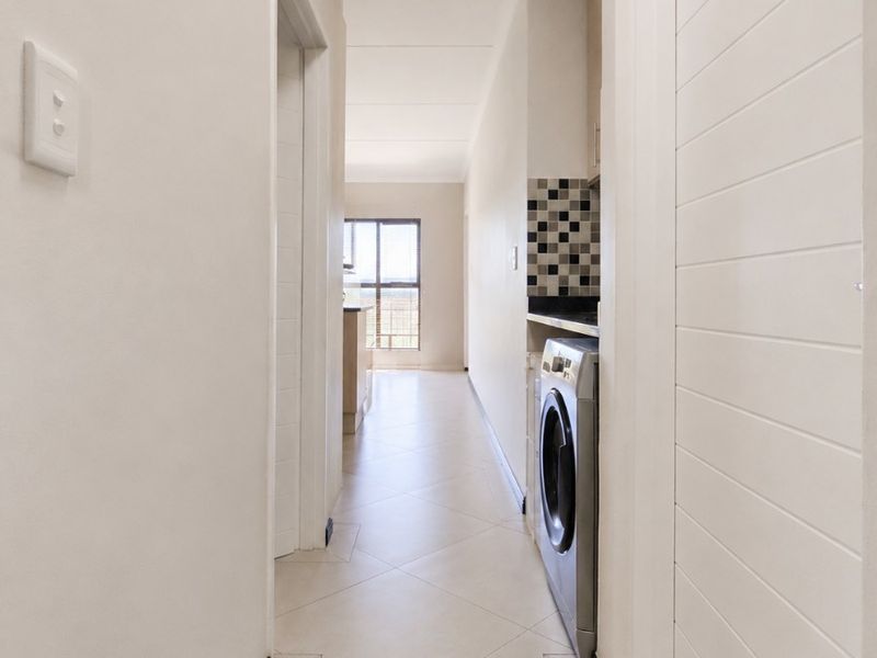 A clean, bright hallway featuring tiled flooring and a convenient built-in laundry nook with mosaic splashback, leading towards an open living area.