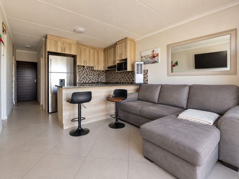 Open-plan living area featuring a modern kitchen with laminate cabinetry, granite countertops, mosaic backsplash, and tiled flooring throughout.