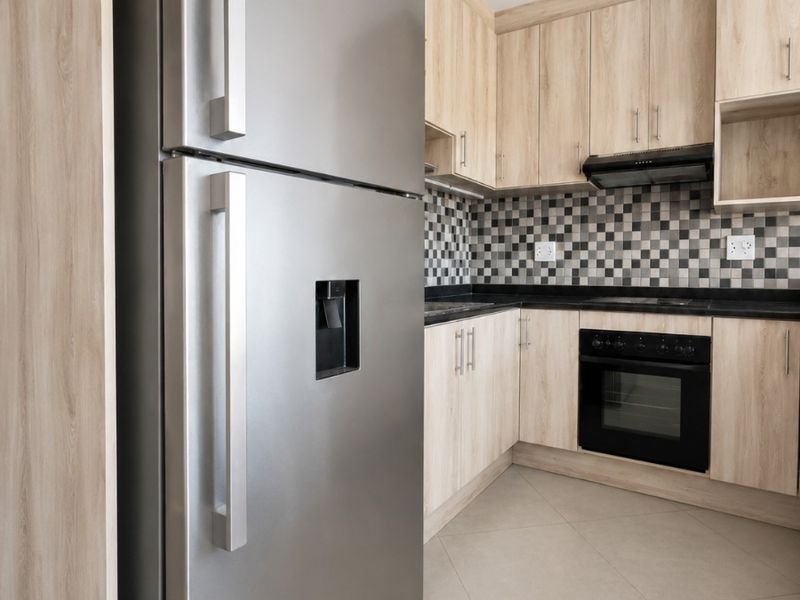 Modern kitchen featuring light wood-finish cabinetry, dark countertops, a tiled backsplash, and integrated appliances including an oven and extractor fan.