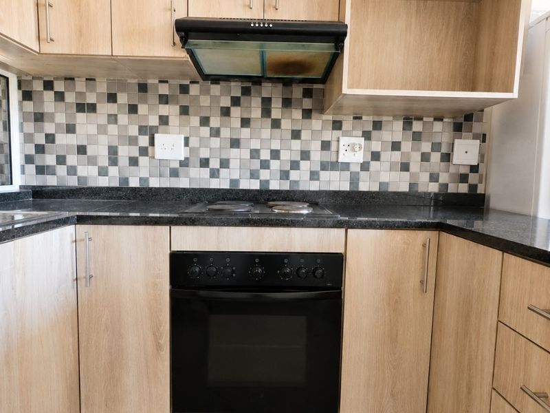 A functional kitchen featuring light wood-finish cabinetry, dark granite countertops, a mosaic tile backsplash, and integrated cooking appliances.