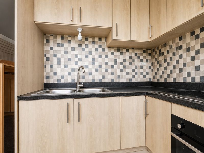 Compact kitchen featuring light wood-finish cabinetry, black granite countertops, a mosaic tile backsplash, and integrated stainless steel sink and oven appliances.