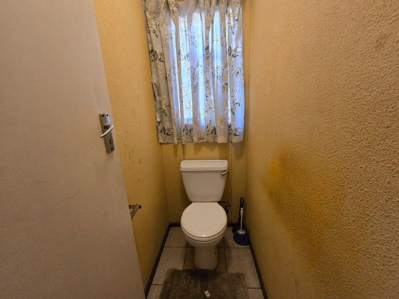 A small guest toilet featuring tiled flooring and textured walls in need of cosmetic updates and repainting.