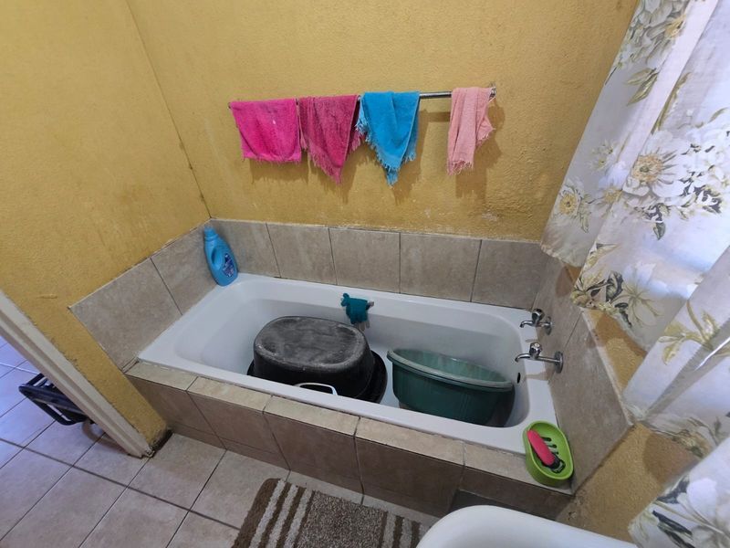 A bathroom featuring a built-in bathtub with chrome fixtures and tiled splashback, requiring cosmetic updates to the wall finishes.