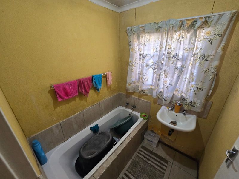 A compact bathroom featuring a bathtub and wall-mounted basin, requiring cosmetic updates and wall repairs to improve the overall condition and aesthetic appeal.