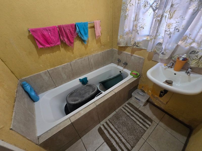 A dated bathroom featuring a built-in bathtub and wall-mounted basin, requiring cosmetic updates and repairs to the wall finishes.