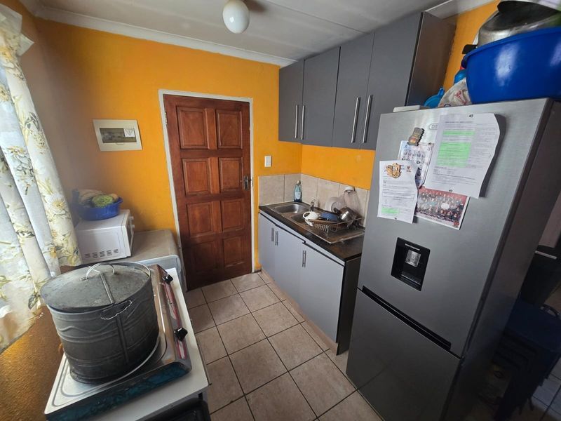 A compact kitchen featuring grey built-in cabinetry, a stainless steel sink, tiled flooring, and a solid wood door.
