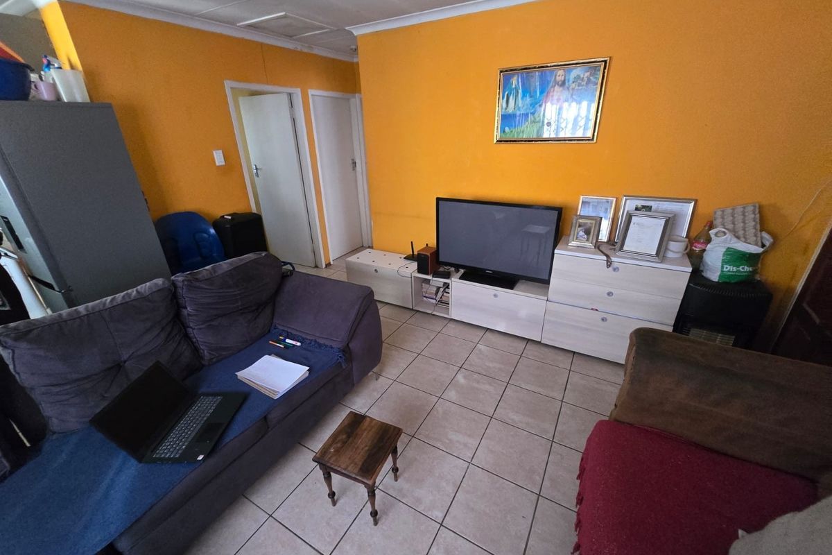 A living room featuring tiled flooring and bright orange walls, offering a functional space that could benefit from cosmetic updates and modern finishes.