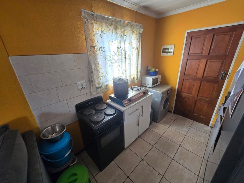 A compact kitchen area featuring tiled flooring, a tiled splashback, and basic cabinetry. The space is functional but would benefit from cosmetic updates.