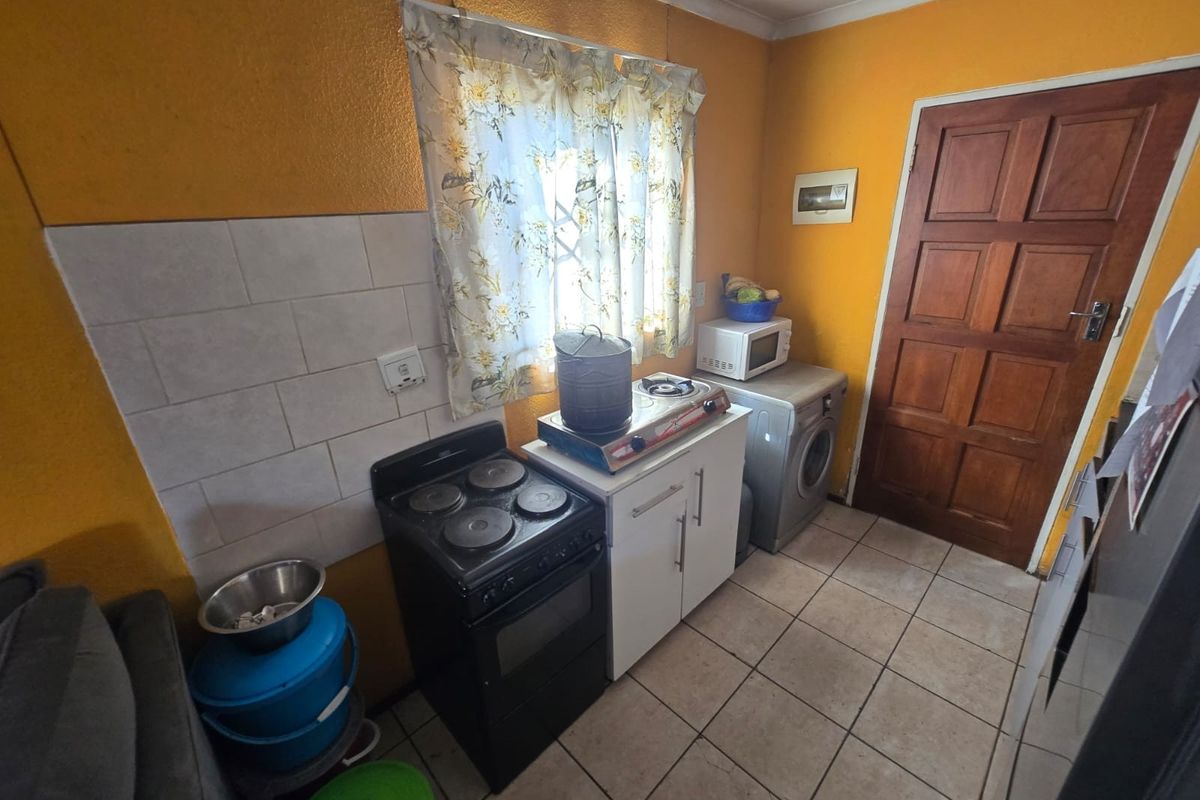 A compact kitchen area featuring tiled flooring, a tiled splashback, and basic cabinetry. The space is functional but would benefit from cosmetic updates.