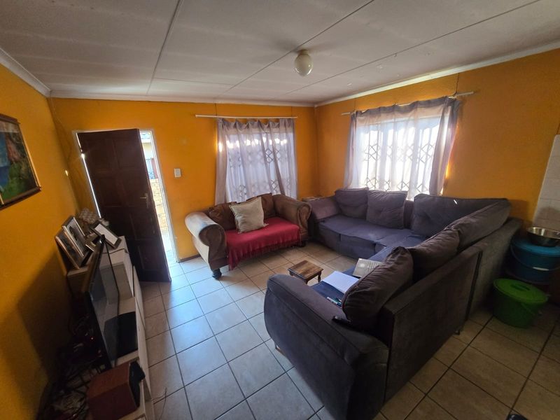 A living room featuring tiled flooring, security gates on windows, and a standard ceiling, providing a functional space with potential for cosmetic updates.
