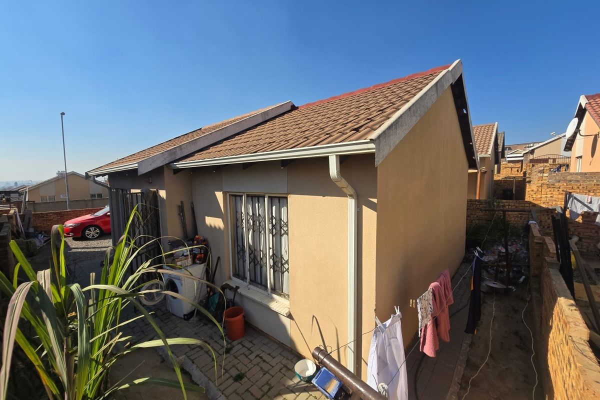 Rear exterior view of the townhouse featuring a tiled roof, paved patio area, and brick boundary walling.