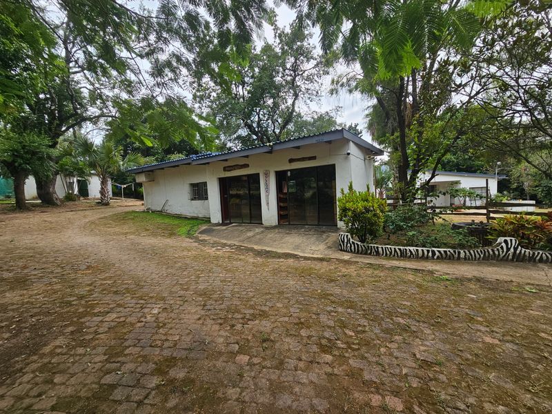 Exterior view of a small holding building featuring a cobblestone driveway, sliding glass entrance doors, and established surrounding trees.