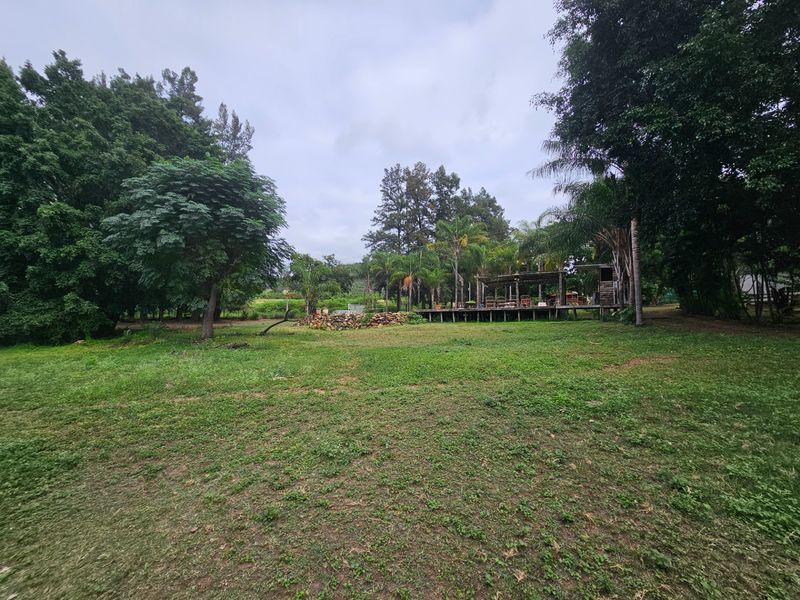 Expansive garden area featuring a large lawn, mature trees, and a raised wooden deck with a pergola structure.