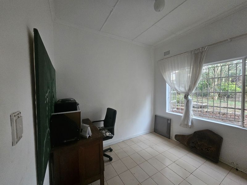 A functional office space featuring tiled flooring and security bars on the window, offering a blank canvas for potential renovation or home office setup.