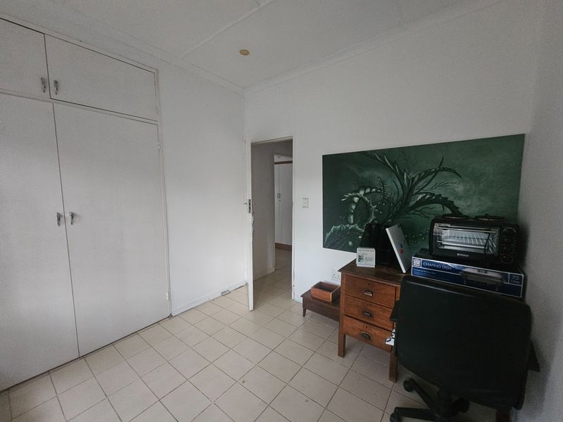 A bedroom featuring built-in cupboards and tiled flooring, offering a functional space with potential for cosmetic updates.