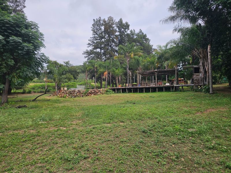 Expansive garden area featuring a raised wooden deck with a pergola structure and a natural stone retaining wall set within a lush landscape.